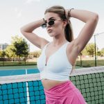 A woman in a white top and pink skirt on a tennis court